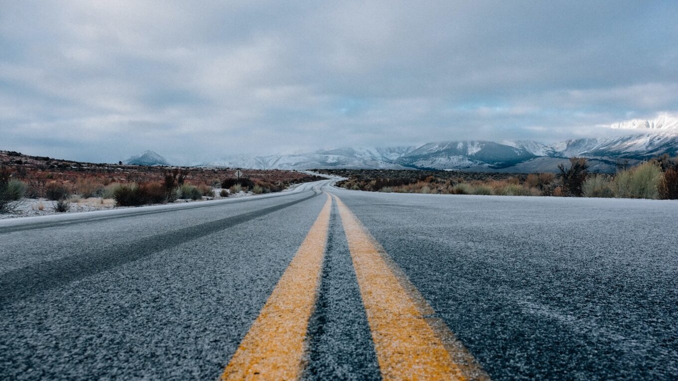 Solid yellow lines between lanes of a frosty road disappearing into the distance, into the mountainour scenery